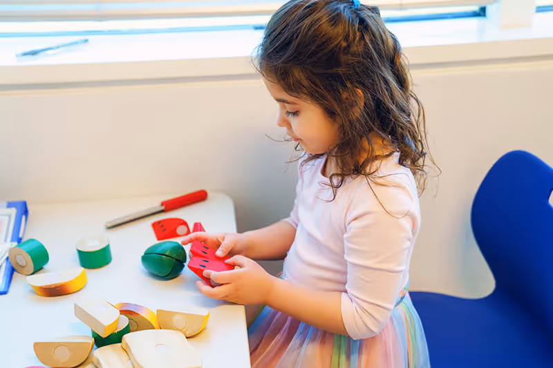 A child joyfully engaging in play therapy with fake food items in a nurturing therapy room at North Shore Pediatric Therapy.