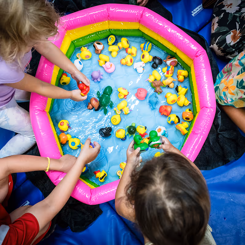 Child engaging together in sensory play at a small blow up pool