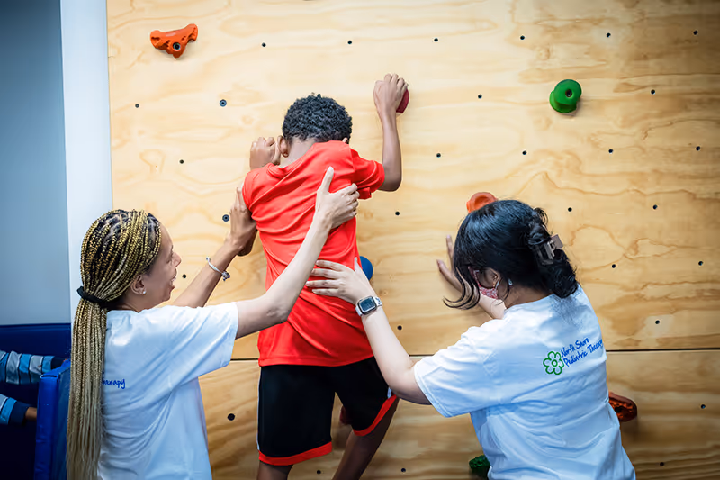 Pediatric therapists in Lincolnwood, IL helping a child on a rock wall in our NSPT center.