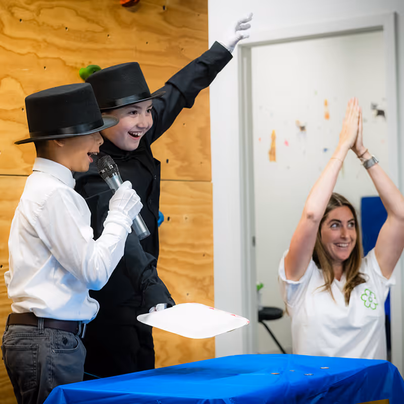 Two children putting on a magic show at the Lincolnwood Open House while their Occupational Therapist looks on and celebrates.