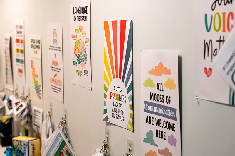 A speech therapy room wall at North Shore Pediatric Therapy with signs encouraging all modes of communication