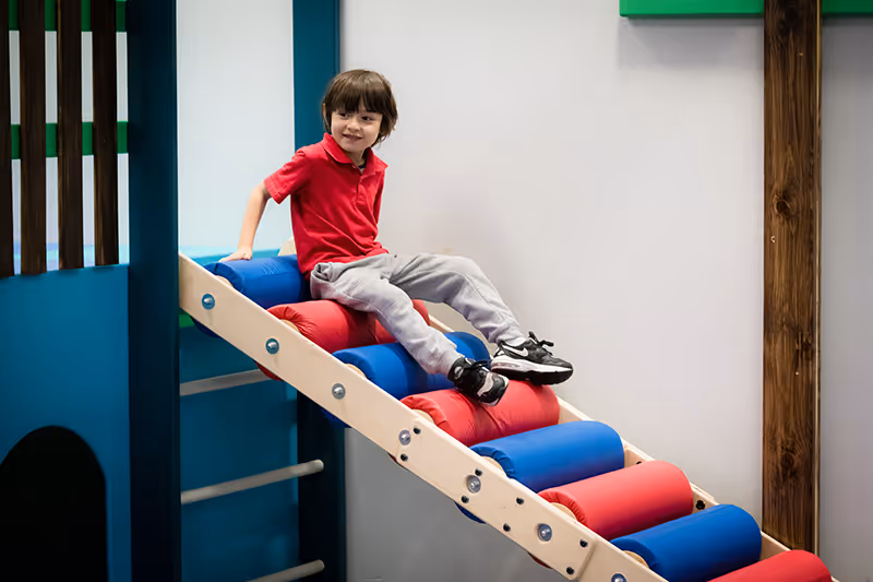A child with a red shirt playing on therapy gym equipment.