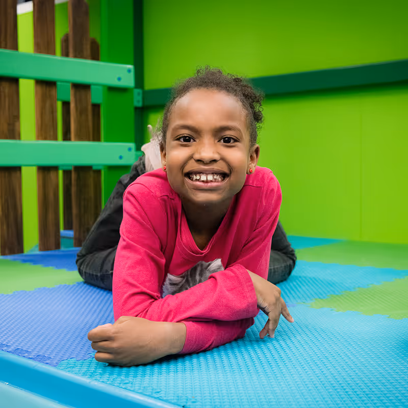 A child smiling while lying down and enjoying the gym space at North Shore Pediatric Therapy in Evanston