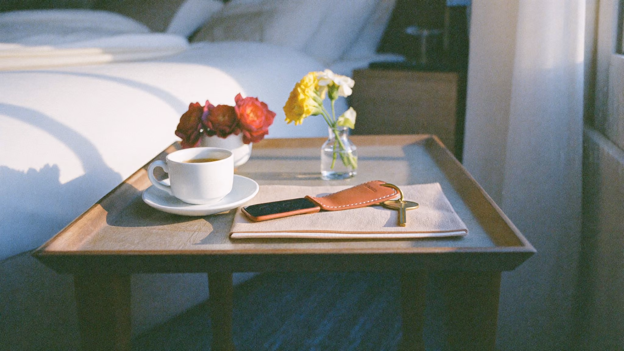 Hotel room key on a table beside a coffee and fresh flowers