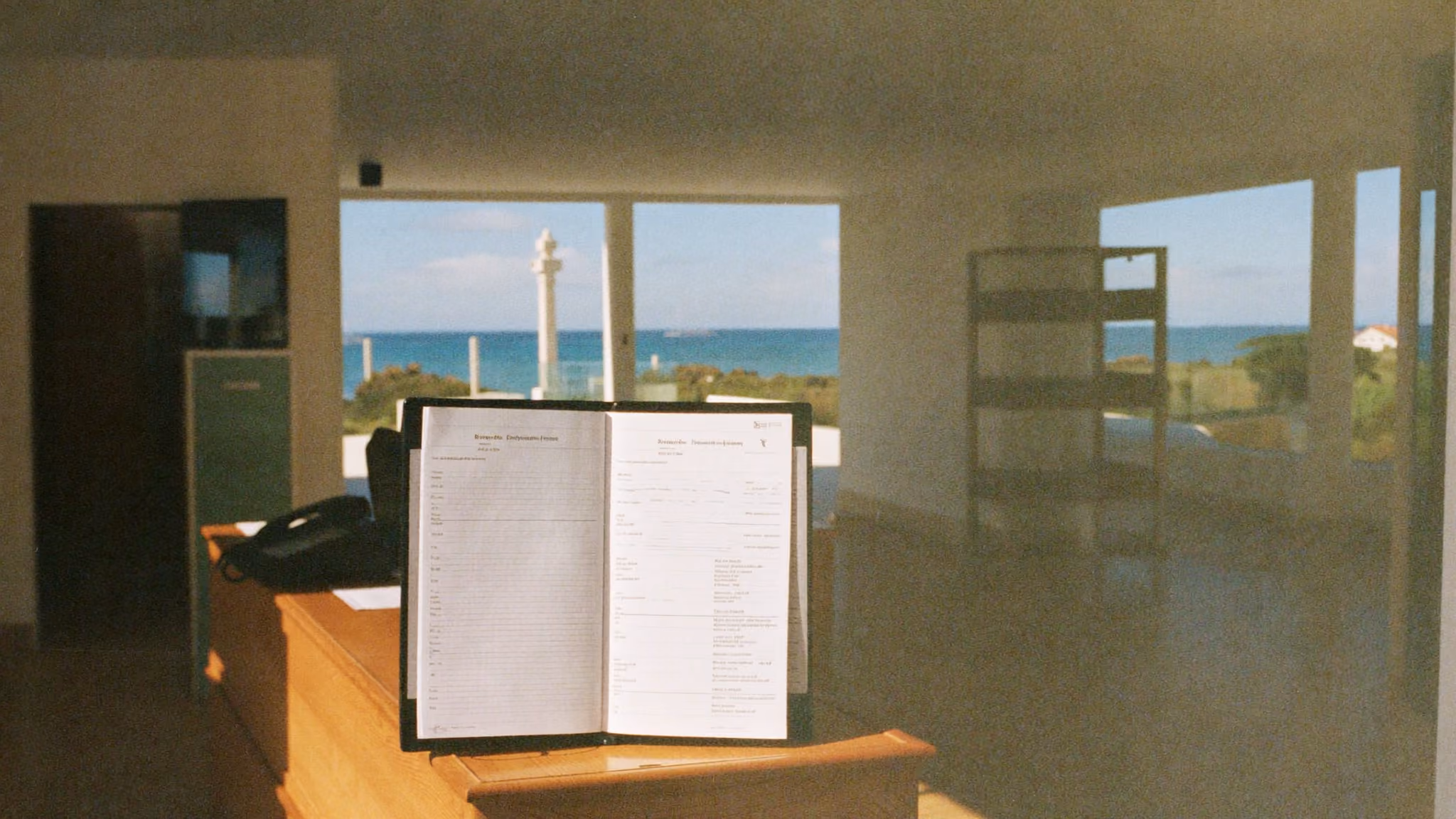 Reception desk of a small hotel at the end of the day, with a landline phone and an open bookings notebook