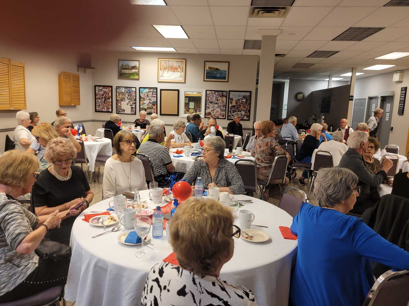 Vue rapprochée d’une autre table remplie de membres de L’Amicale, entourés d’une décoration de fête aux couleurs bleu-blanc-rouge.
