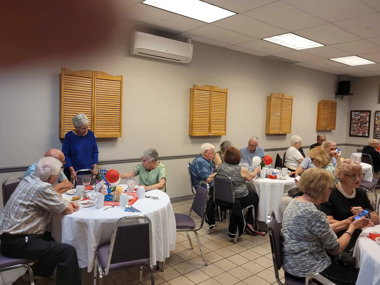 Une vue de la salle où plusieurs tables sont remplies de membres souriants. Une ambiance festive et conviviale règne dans la pièce.