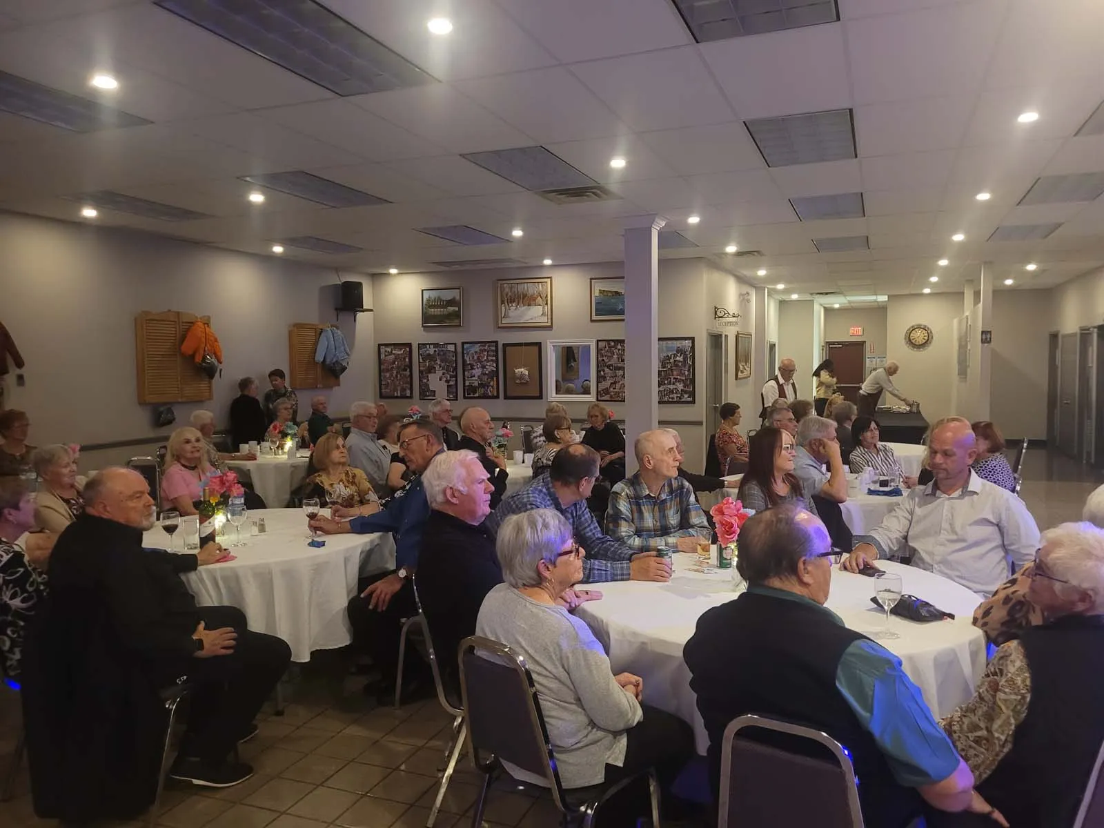 Vue de la salle remplie de membres de L’Amicale assis aux tables rondes, attentifs à la performance musicale sur scène.