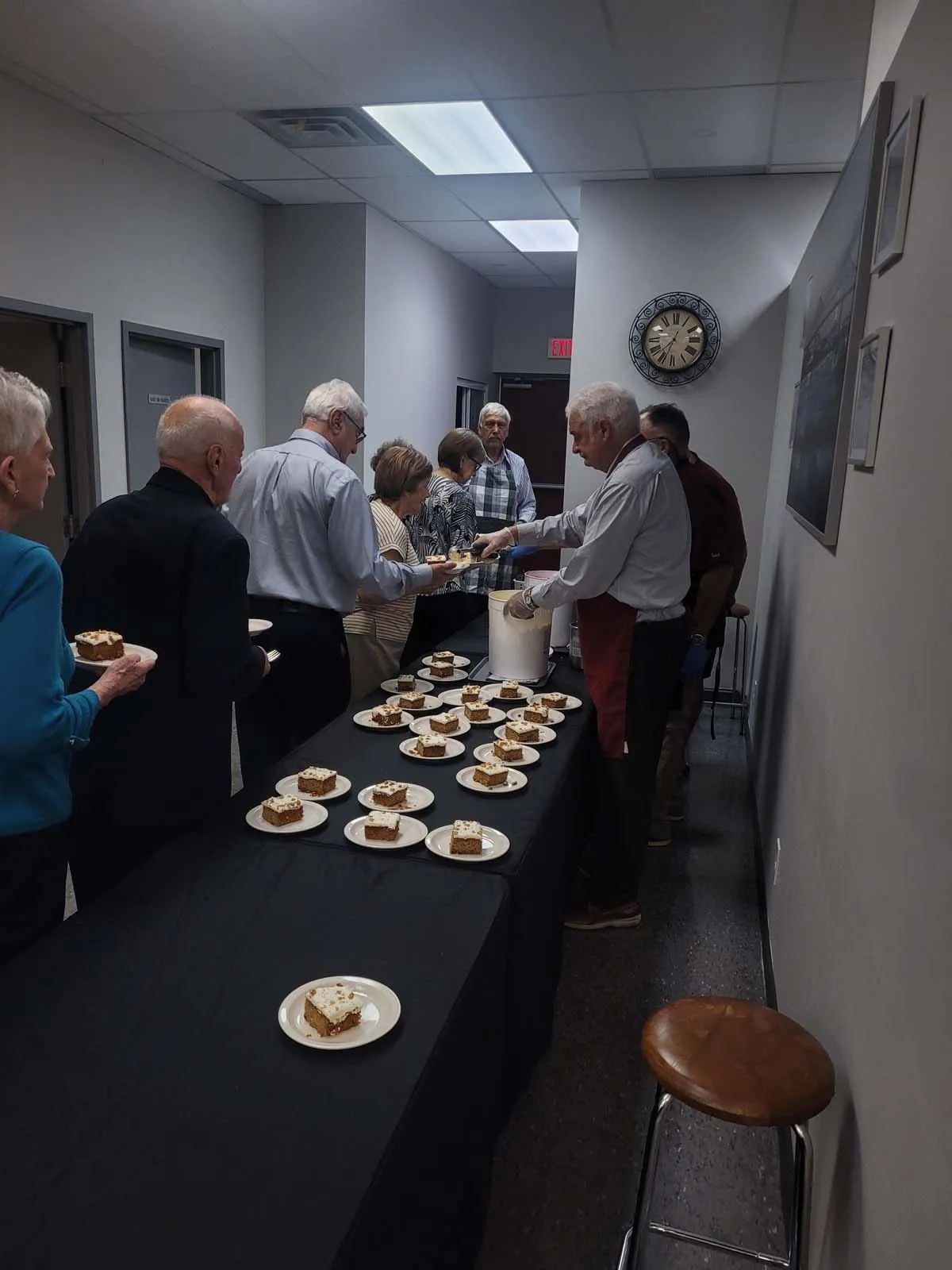 Distribution de desserts sur une table noire, avec plusieurs assiettes de gâteau déjà préparées, pendant que les membres patientent.