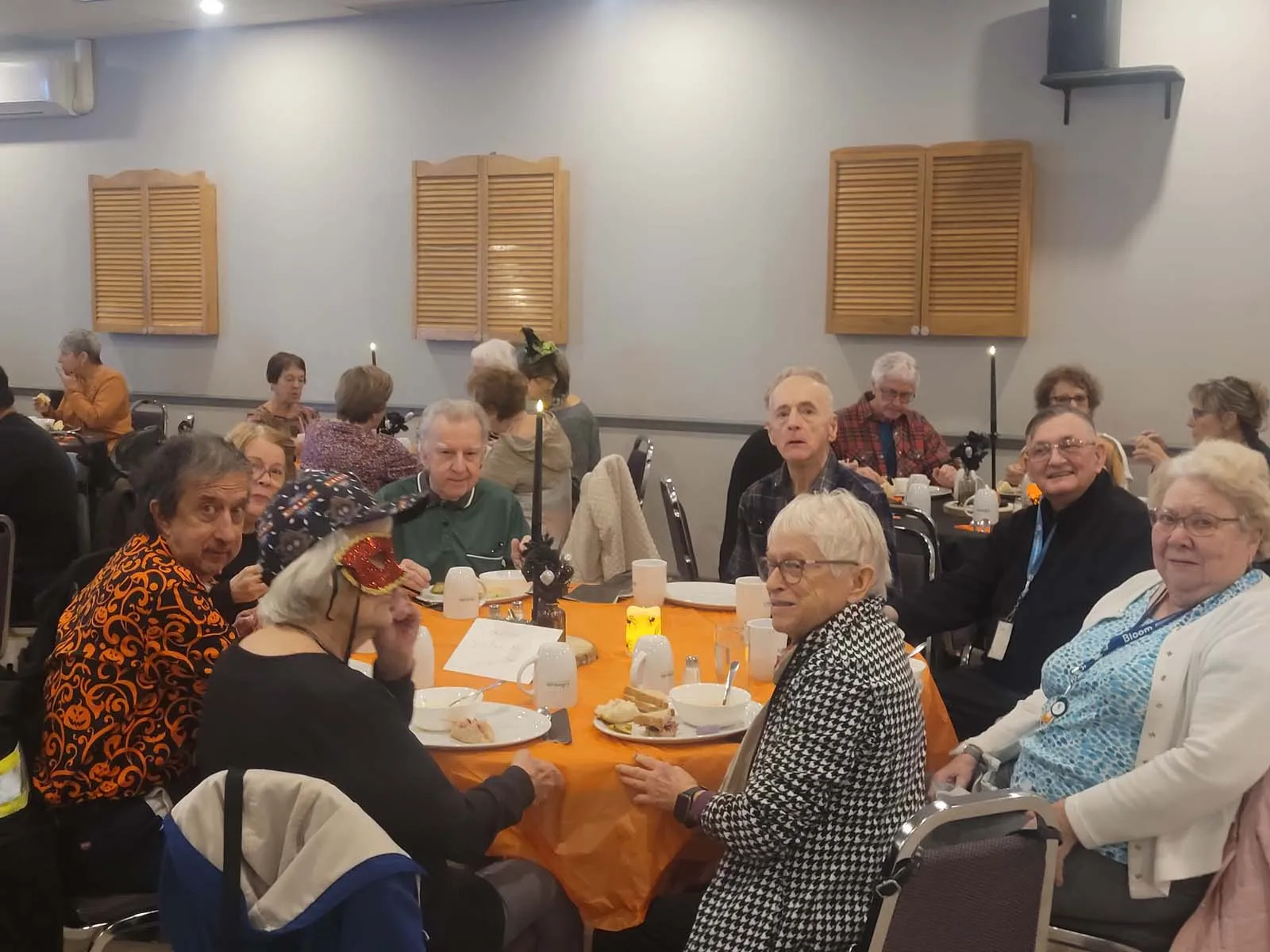 Groupe de membres réunis à une table décorée, plusieurs portant des chapeaux ou accessoires d’Halloween. Ambiance chaleureuse et détendue pendant le repas.
