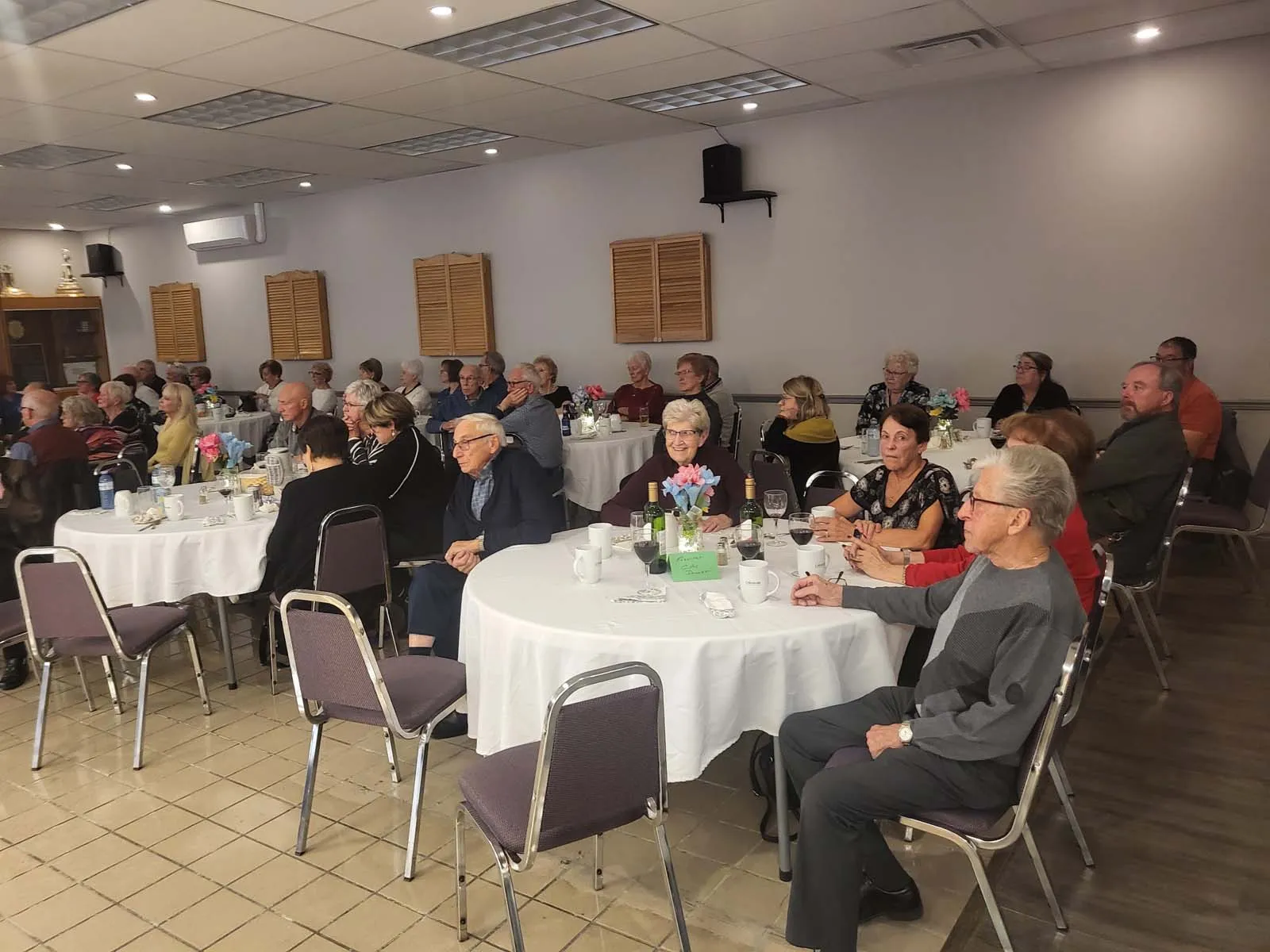 Même scène que l’image précédente : convives attentifs face à une scène, lors d’un événement communautaire.