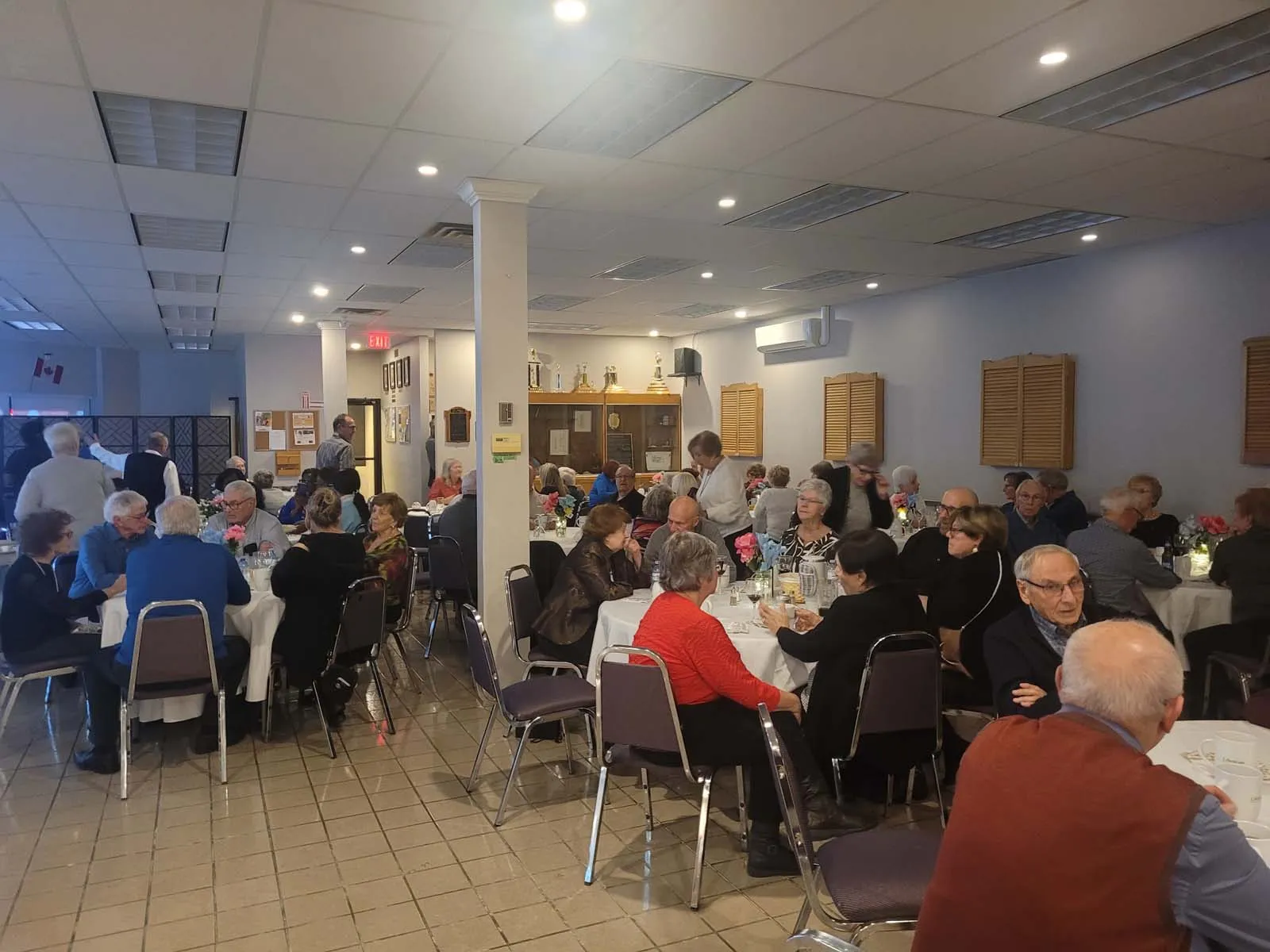 Nombreuses personnes âgées assises à des tables décorées, profitant d’un repas dans une ambiance chaleureuse et festive.