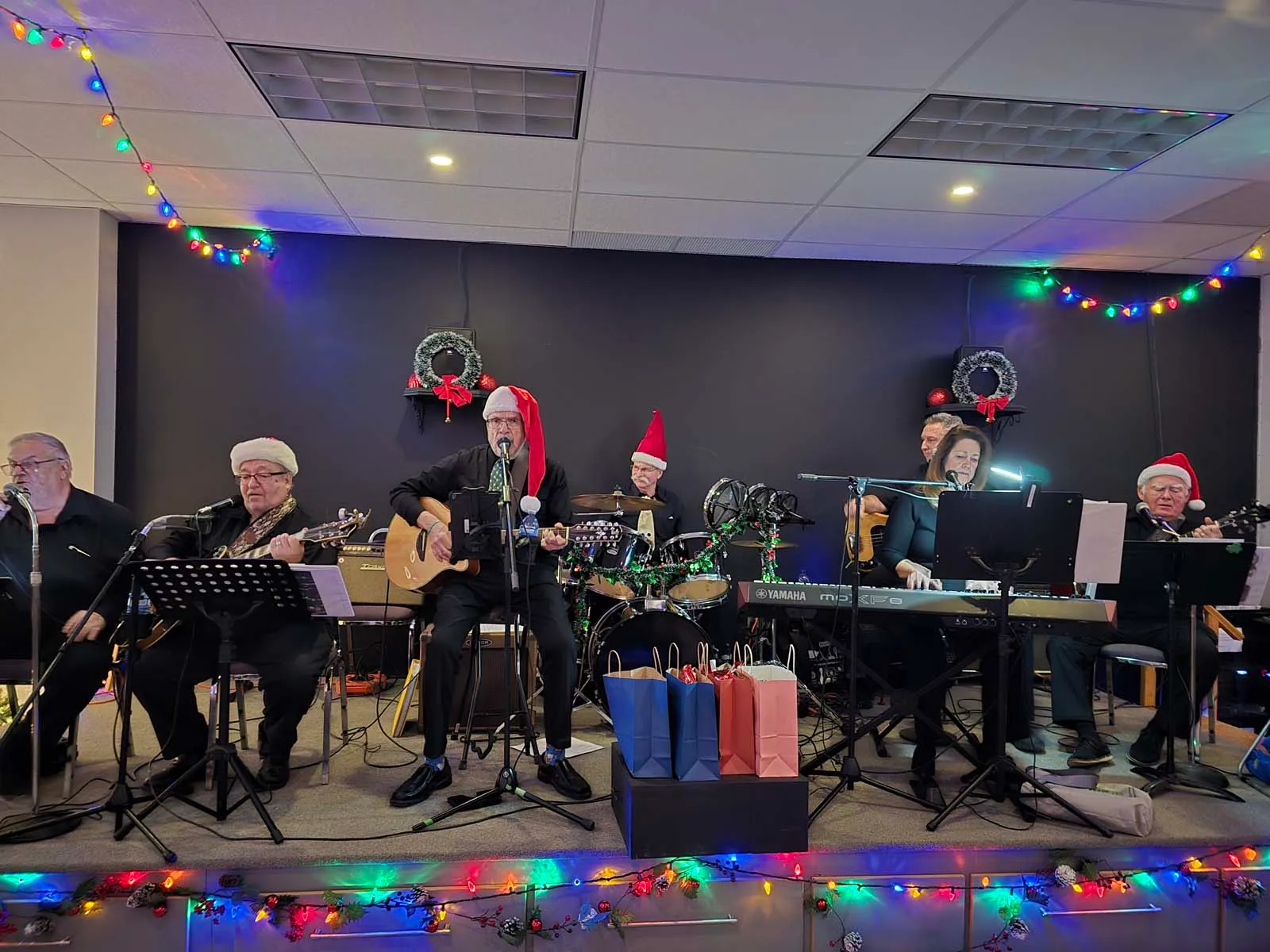 Groupe de musiciens membres de L’Amicale sur scène, jouant de la musique en direct, décorés de chapeaux et ornements festifs.