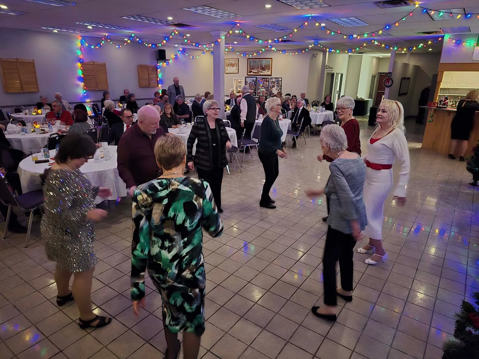 Membres de L’Amicale dansant sur la piste, entourés de tables et de lumières festives, pendant l’animation musicale de l’événement.