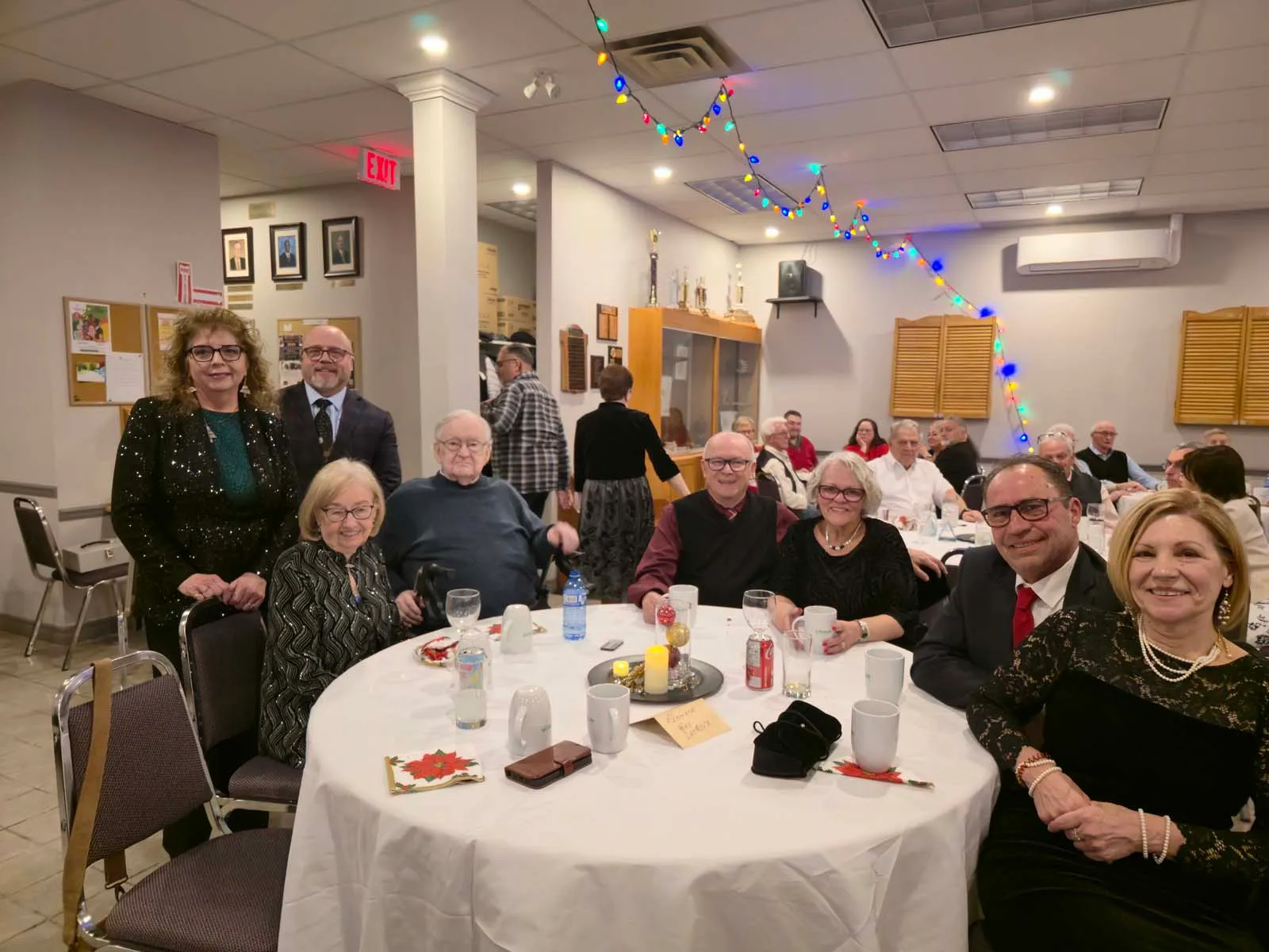 Grand groupe de membres de L’Amicale rassemblés autour d’une table, posant pour une photo souvenir pendant la soirée.