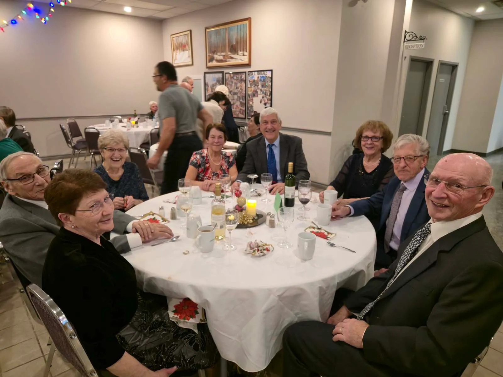 Huit membres réunis autour d’une grande table, partageant un moment de convivialité avec vin, chandelles et décorations festives.