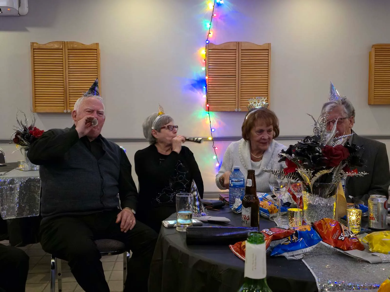 Membres de L’Amicale assis autour d’une table, portant des chapeaux festifs et célébrant le Nouvel An dans une ambiance conviviale.