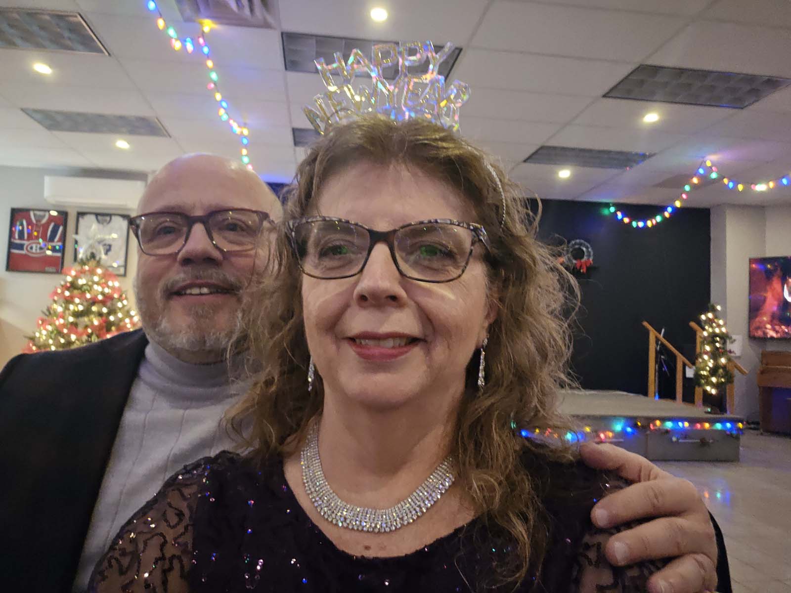 Deux membres de L’Amicale posant ensemble pour un égoportrait, souriant devant la scène décorée et les lumières festives.