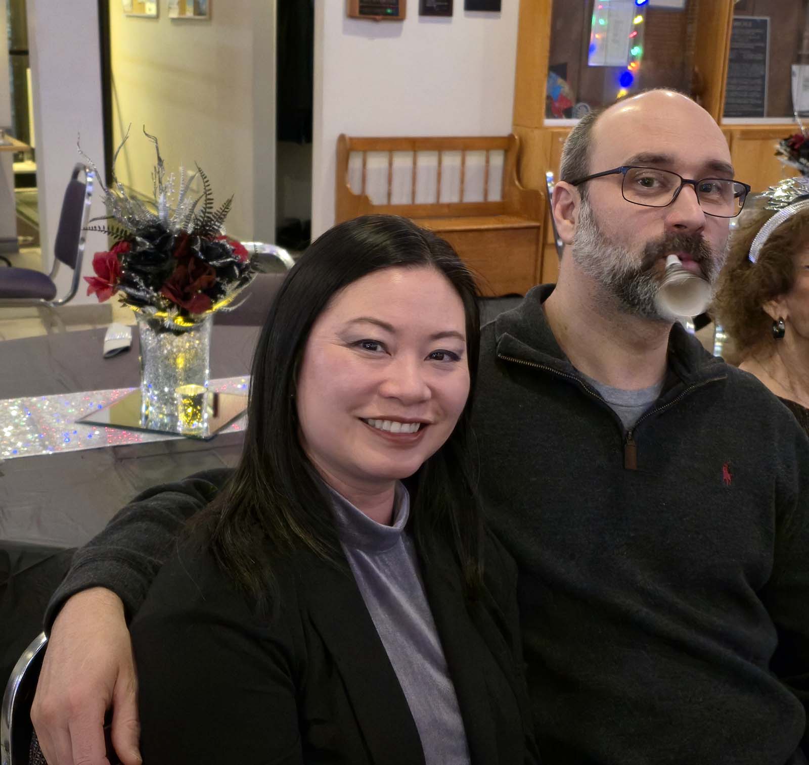 Deux membres de L’Amicale posant ensemble, souriants et détendus, assis à une table décorée pour la soirée.