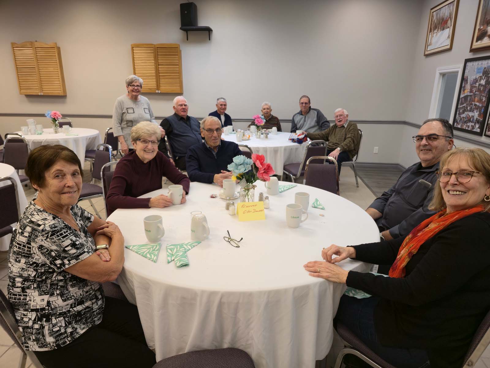 Plusieurs membres de L’Amicale réunis autour de tables, échangeant et profitant du repas dans une atmosphère chaleureuse.