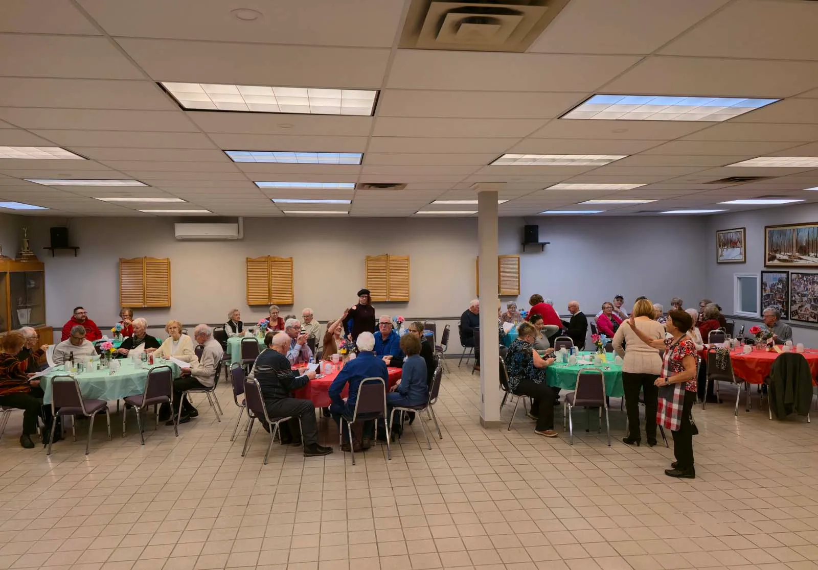 Vue panoramique de la salle de L’Amicale, avec plusieurs tables de membres assis et échangeant lors d’un repas communautaire.