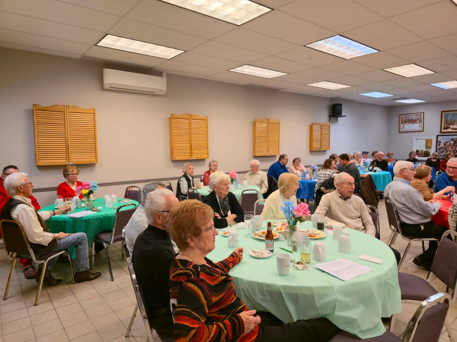 Plusieurs membres de L’Amicale réunis dans la salle, discutant et profitant du repas communautaire.
