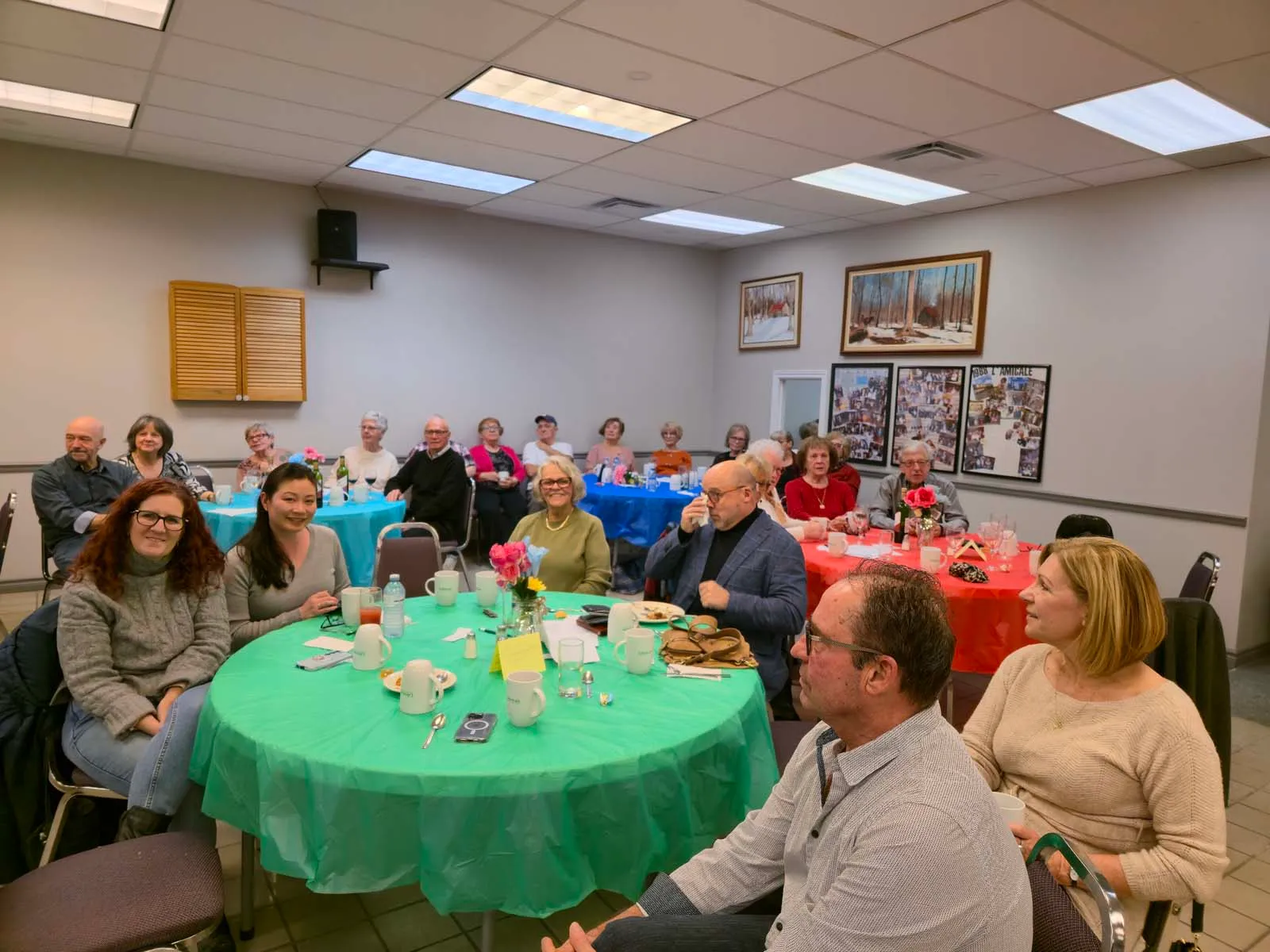 Vue d’ensemble des tables de L’Amicale, avec des membres attentifs assis et regardant vers l’avant de la salle.