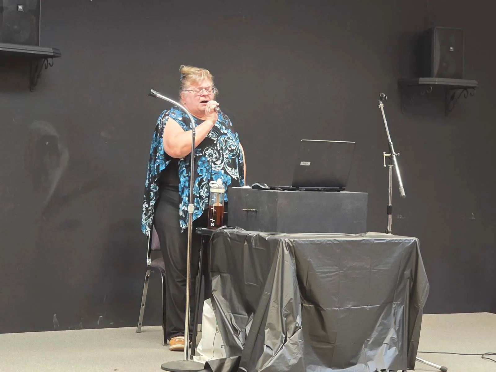 Membre de L’Amicale chantant au micro sur scène lors d’une soirée sociale, accompagnée d’un poste audio.