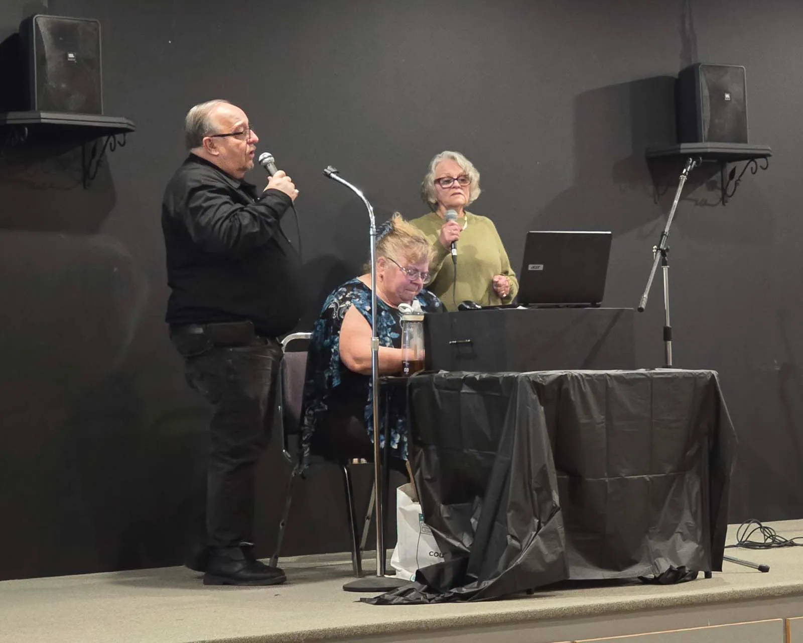 Trois membres de L’Amicale interprétant une chanson sur scène lors d’une activité sociale.