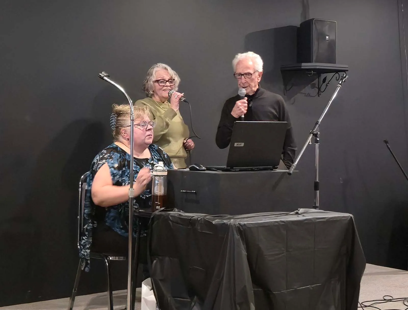 Trois membres de L’Amicale chantant ensemble sur scène lors d’une soirée musicale.