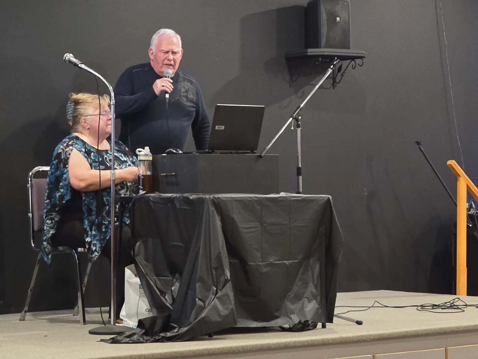 Membre de L’Amicale prenant la parole au micro sur scène lors d’une activité communautaire.