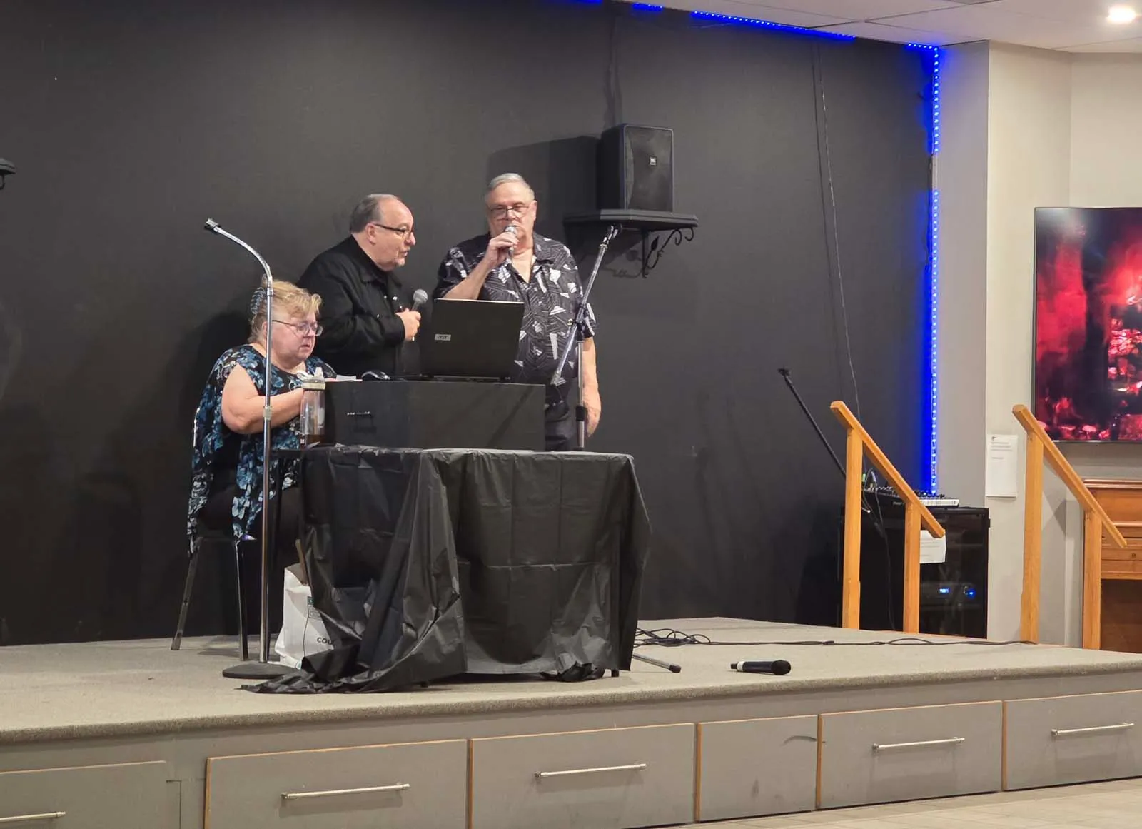 Des membres de L’Amicale animent la soirée sur scène avec micros et équipement audio.