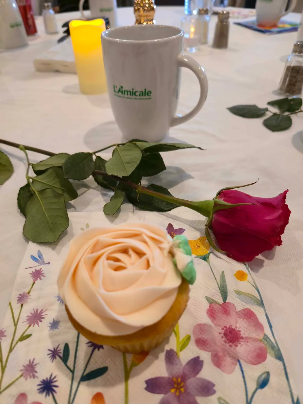 Rose, tasse de l’Amicale et petit gâteau décoré sur une table du brunch de la Fête des Mères.