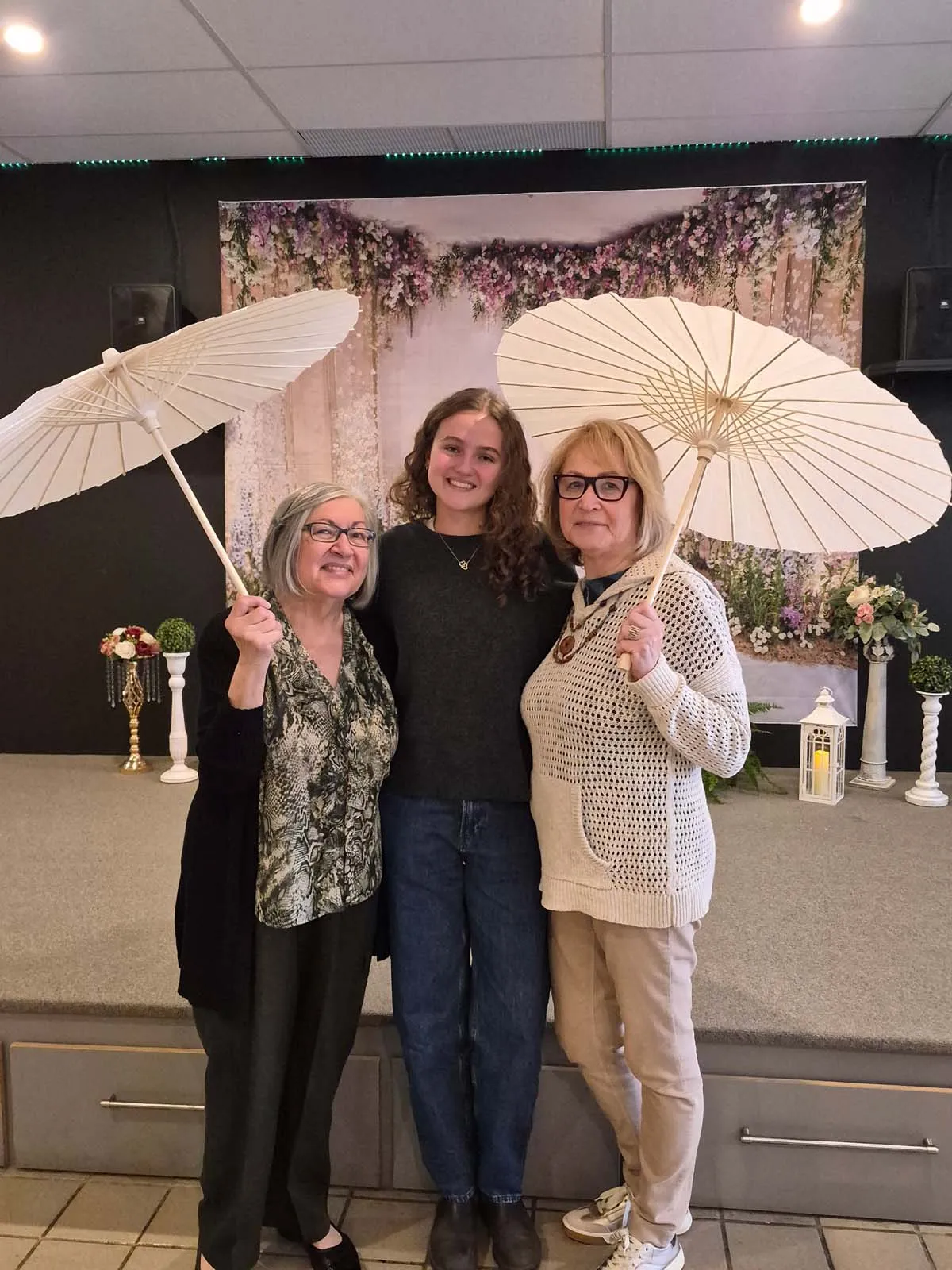 Trois participantes posant avec des parasols devant le décor du brunch de la Fête des Mères de l’Amicale.