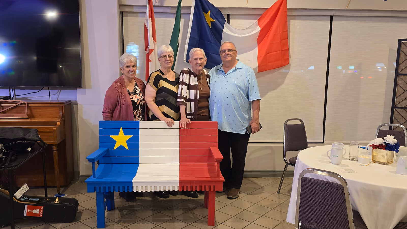 Quatre membres posent derrière le banc peint aux couleurs du drapeau acadien lors de la Soirée acadienne.