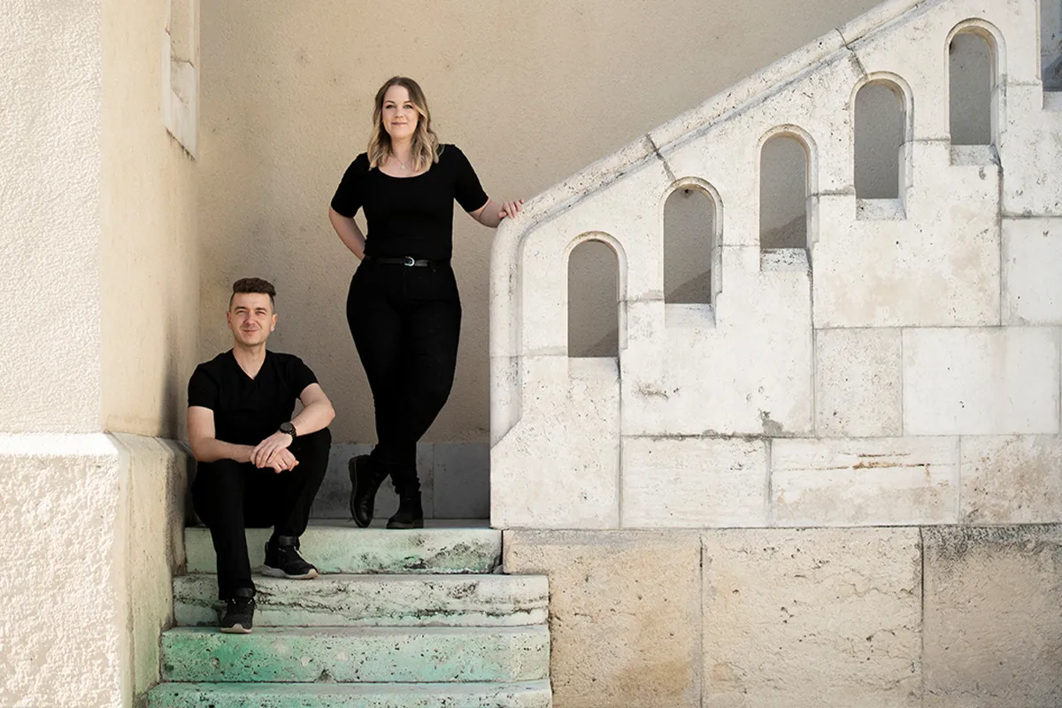 Fanni Zámbó and István Zámbó of Dare Studio on green steps beside a historic building
