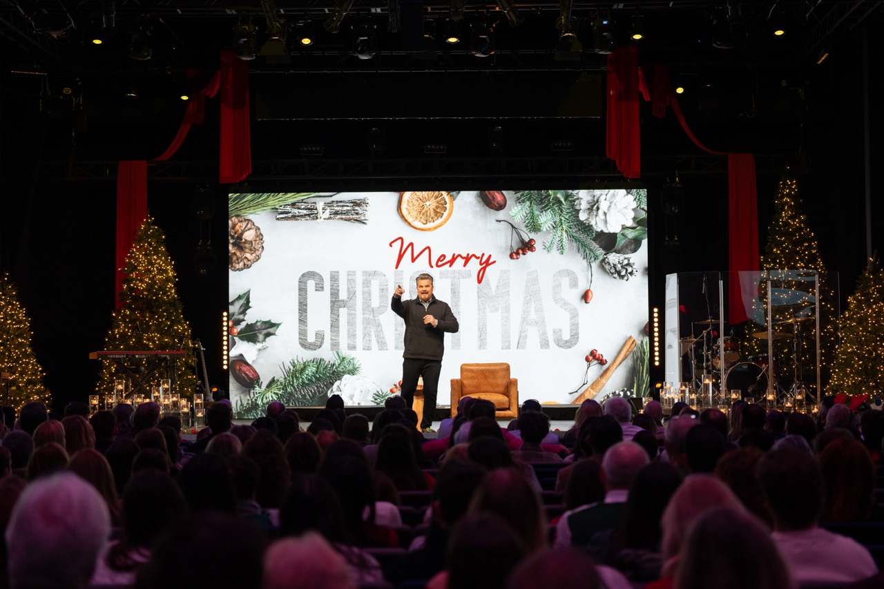 Pastor Tim on stage with merry Christmas banner in the backdrop