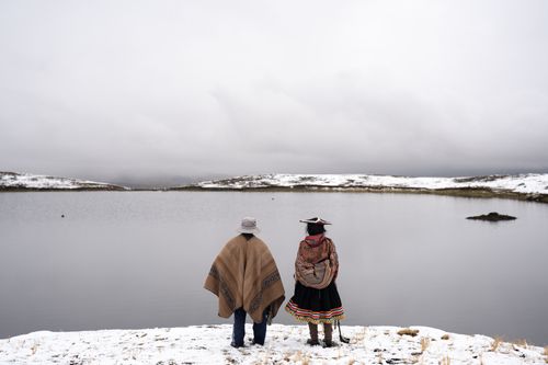 Two people stand on snow and ice overlooking a body of water