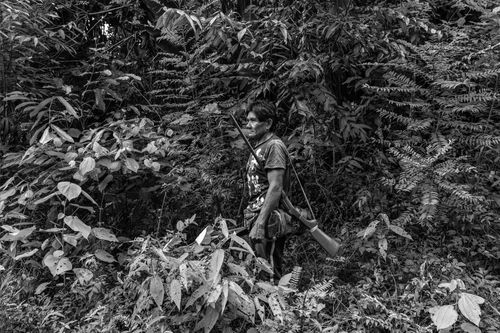 A man stands in a forest with a gun over his shoulder.