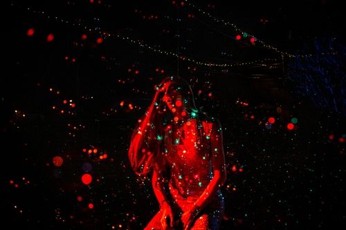 A drag queen performs in the dark with red specks of light.
