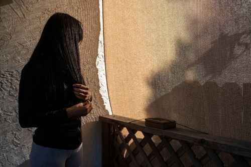 A woman with long hair turns her face away from the camera against a beige background