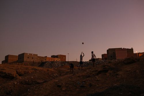 Two boys toss a ball into the air at sunset.