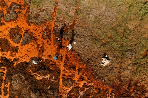 an aerial view of a muddy field of orange water and researchers collecting samples.