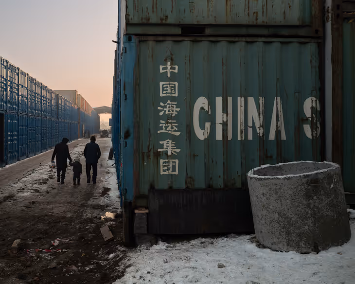 Three people walk past a large shipping container with the word “China” written across it. 