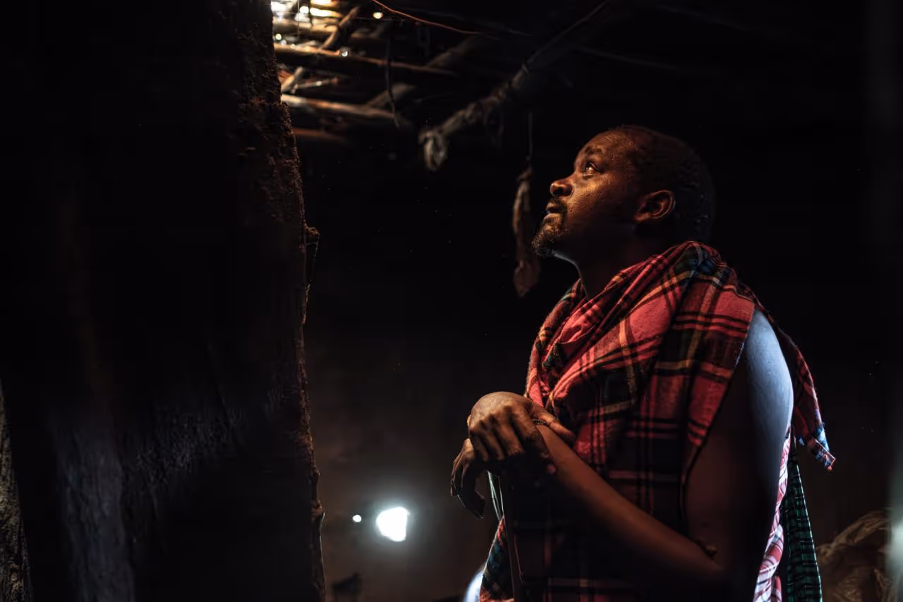 A man standing in a dark room looks upward at a light.