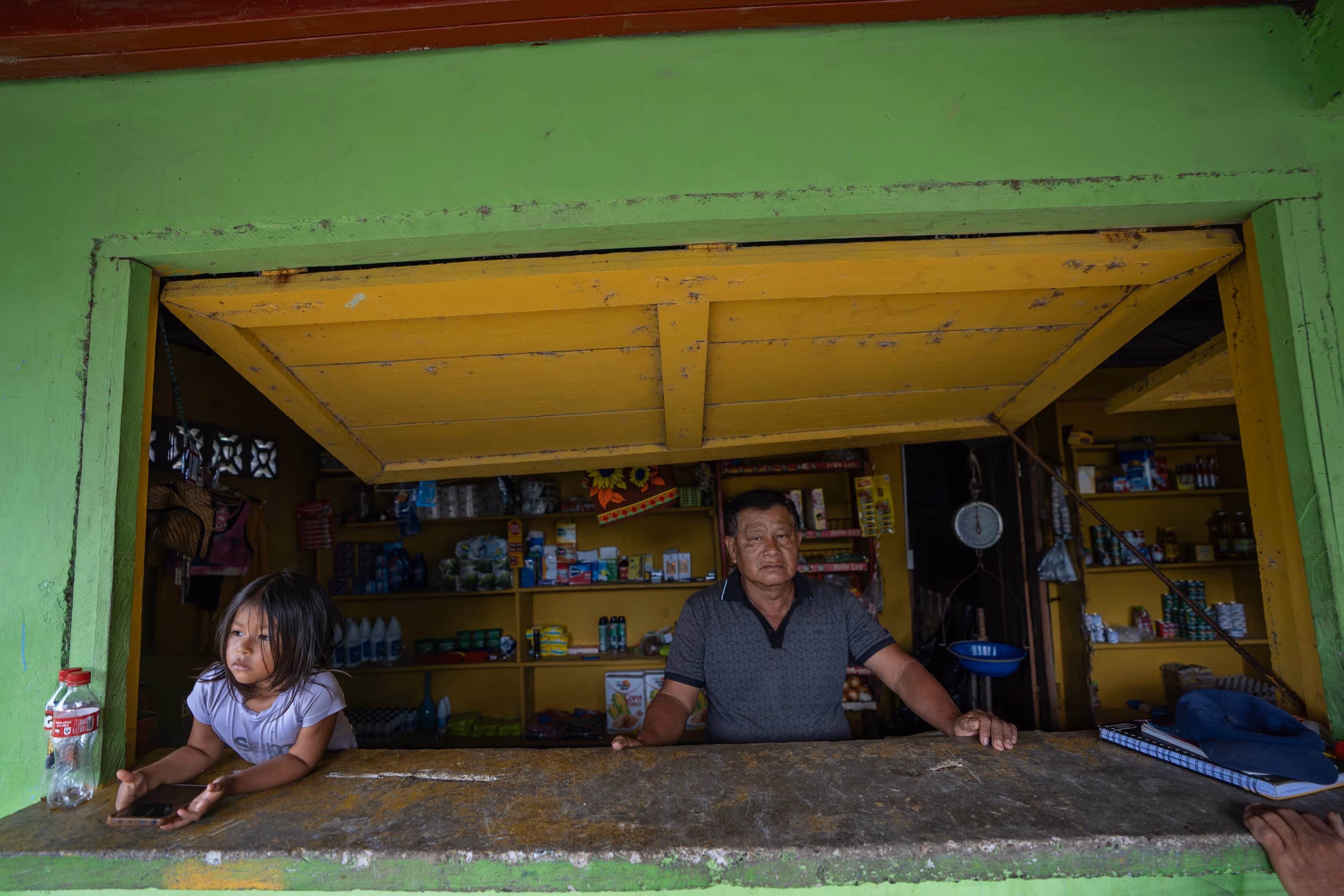 A man and a young girl look out the window of their small store.