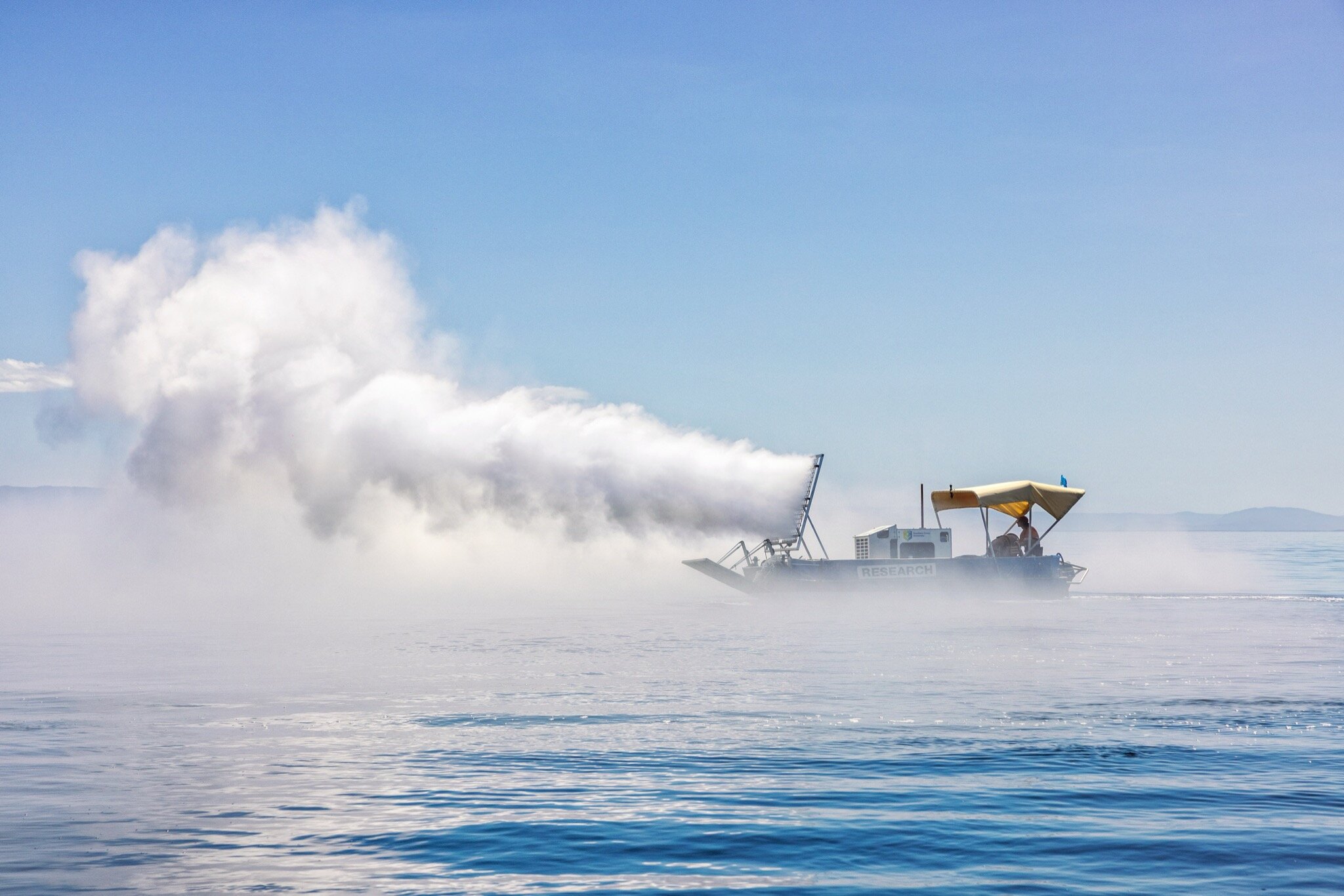 A large cloud of mist trails behind a boat on the ocean.