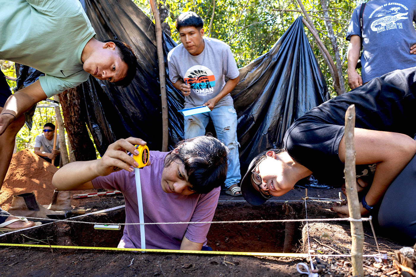 Four young people work on an excavation project in a wooded area.
