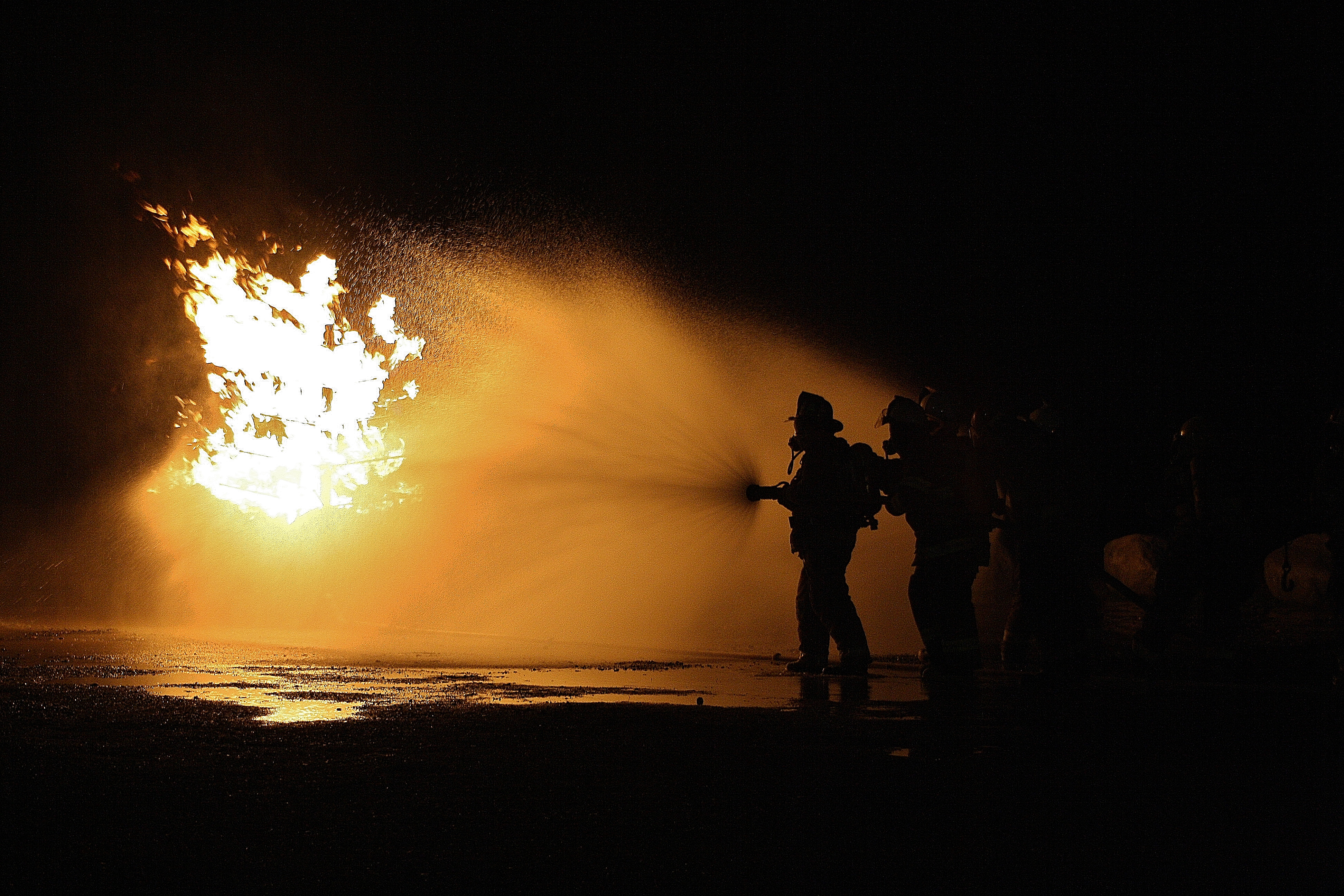 In a dark scene, a firefighter uses a hose to put out a small fire. 