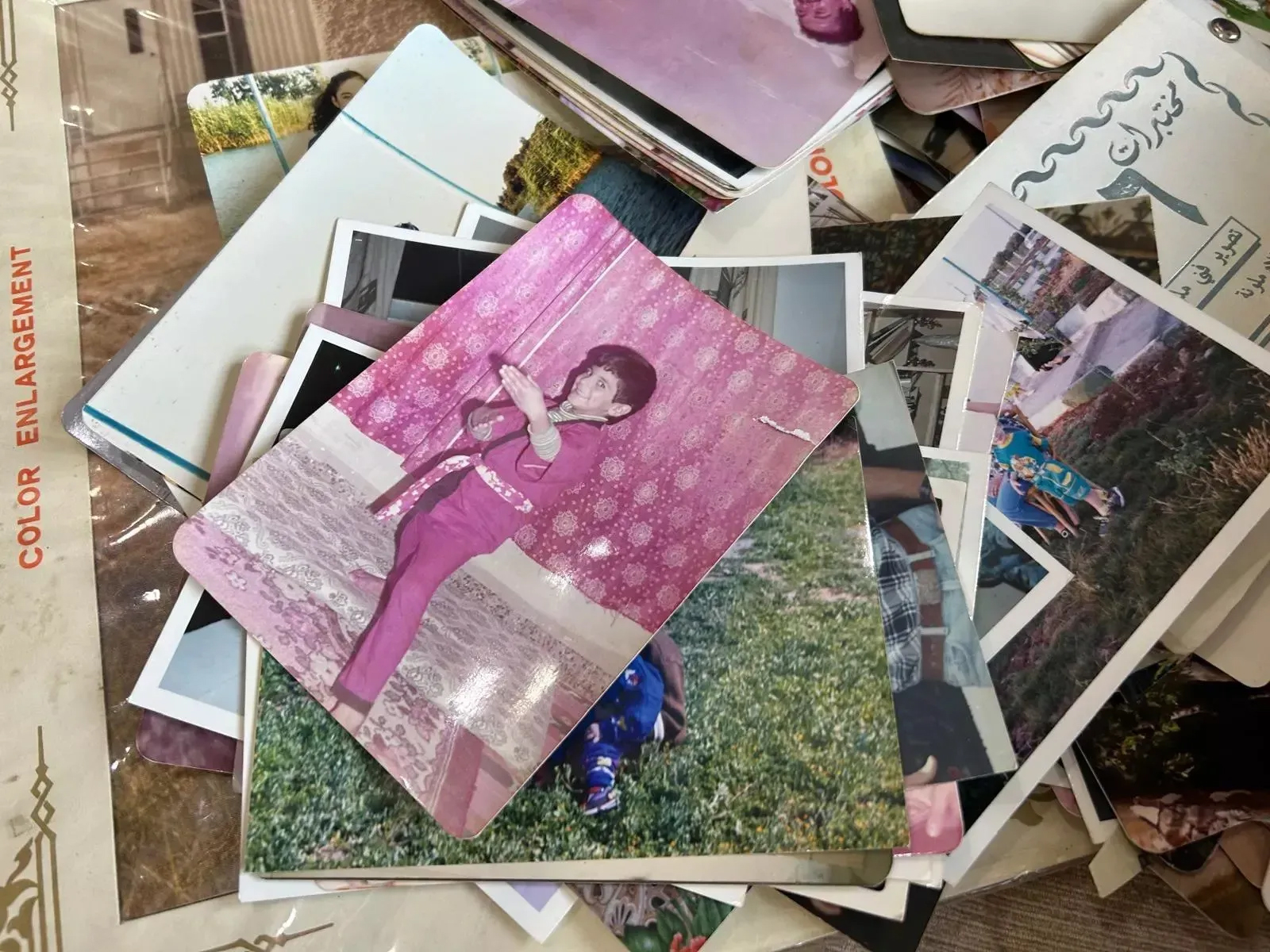 A pile of old photographs. In the image on top of the pile, a young boy poses in a martial arts stance.
